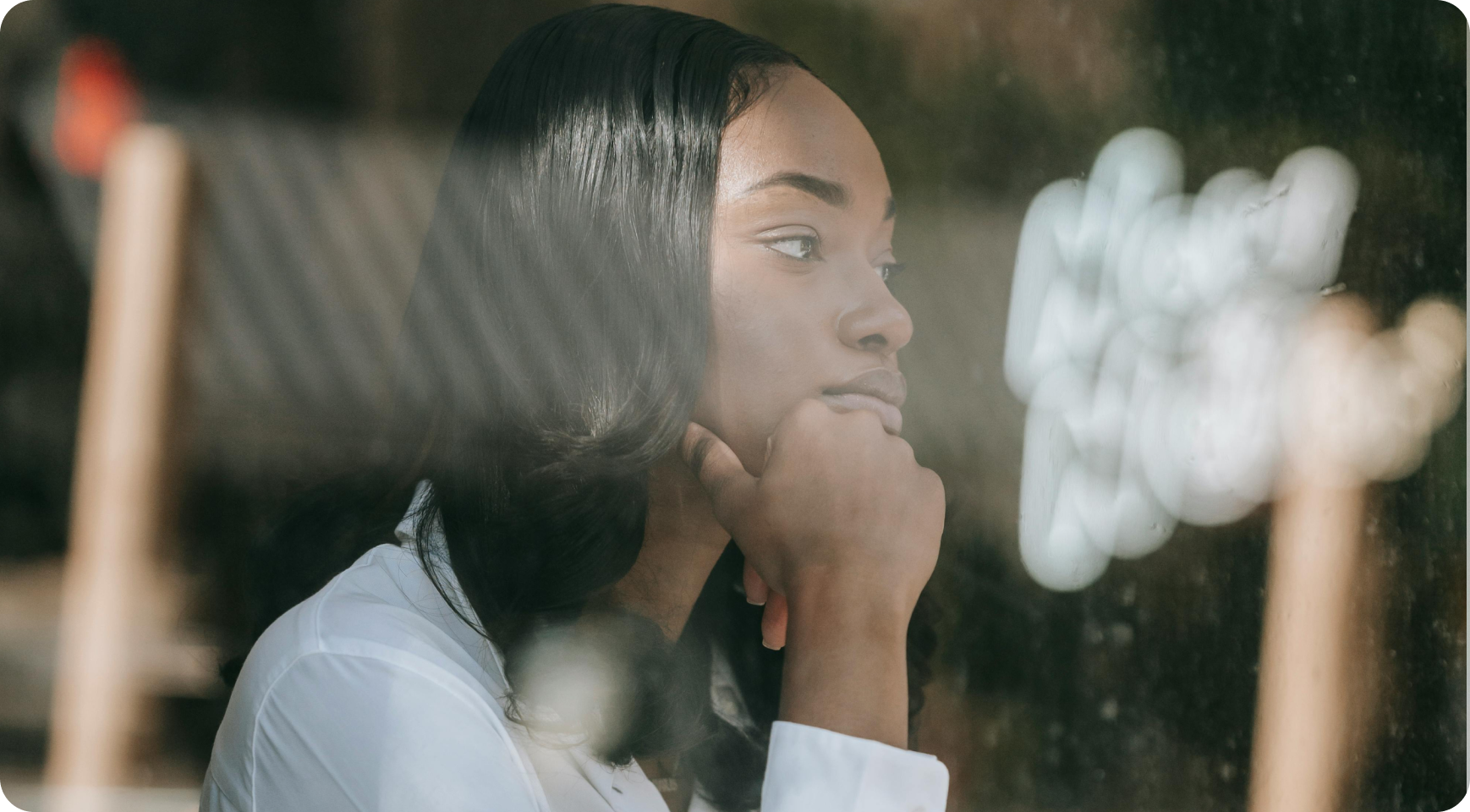 A woman sitting thoughtfully by a window grieving the loss of a loved one